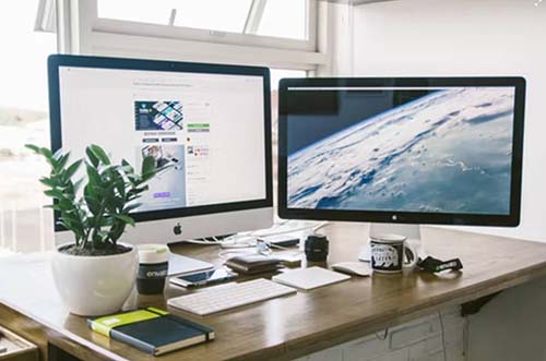 A dual monitor setup on a brown desk. photo – Free.jpg